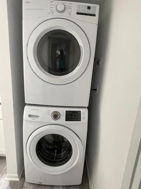 washroom with stacked washer and clothes dryer, wood finished floors, baseboards, and laundry area