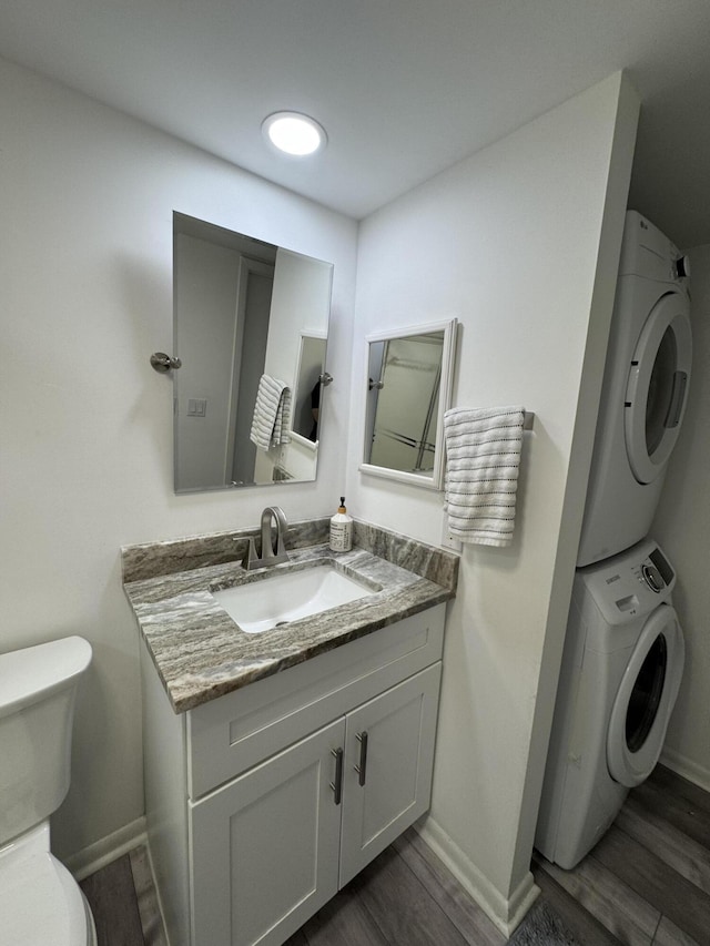 bathroom featuring stacked washer and dryer, wood finished floors, baseboards, and toilet