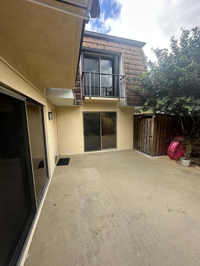 rear view of property featuring a patio area, mansard roof, a balcony, and stucco siding