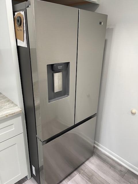 interior details with white cabinets, light wood-type flooring, light stone countertops, baseboards, and stainless steel refrigerator with ice dispenser