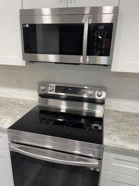 interior details with stainless steel appliances, decorative backsplash, white cabinetry, and light stone counters