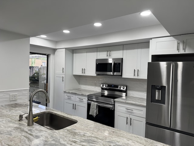 kitchen with appliances with stainless steel finishes, white cabinets, a sink, and light stone counters