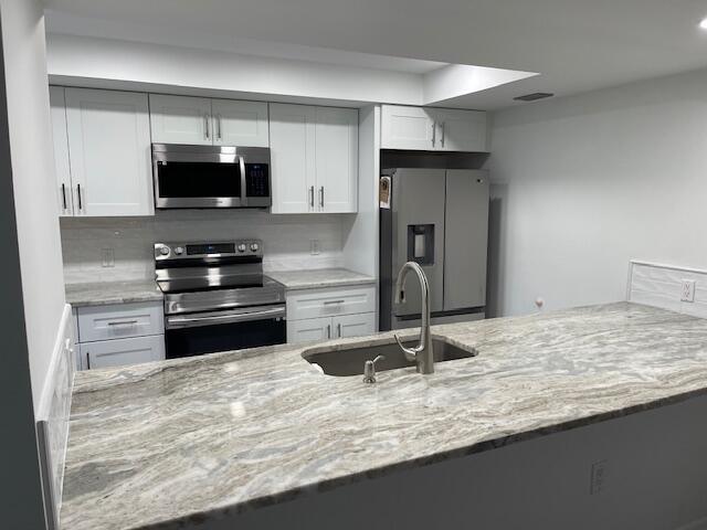 kitchen with white cabinets, appliances with stainless steel finishes, light stone counters, and a sink
