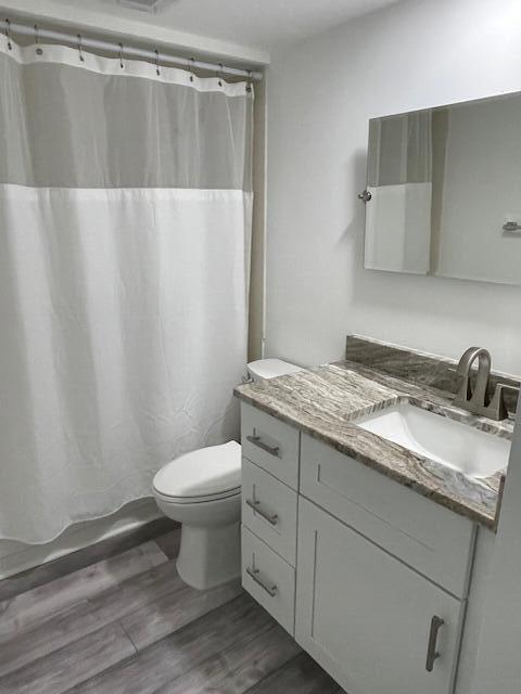 bathroom with wood finished floors, toilet, vanity, and shower / bathtub combination with curtain