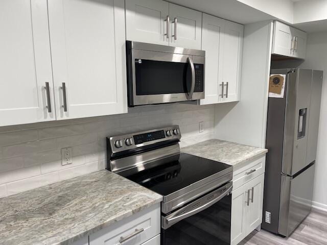 kitchen with appliances with stainless steel finishes, light stone countertops, tasteful backsplash, and white cabinetry