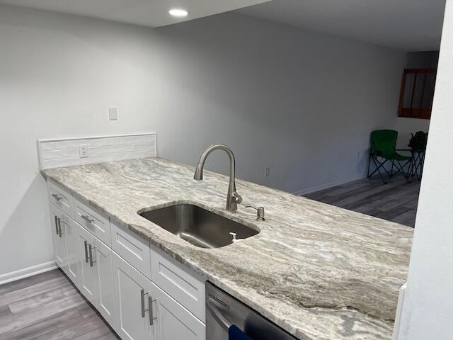 kitchen featuring a sink, light wood-type flooring, recessed lighting, white cabinetry, and light stone counters
