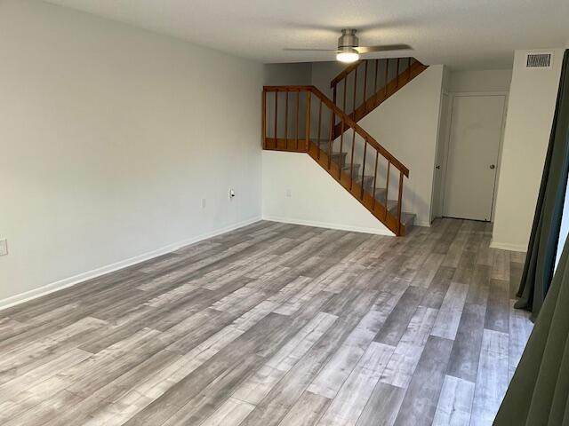 unfurnished living room with visible vents, baseboards, a ceiling fan, wood finished floors, and stairs