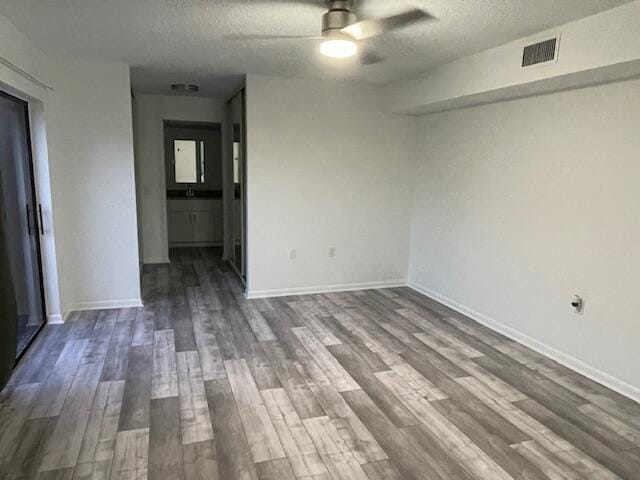 empty room with dark wood-style floors, visible vents, baseboards, a textured ceiling, and ceiling fan