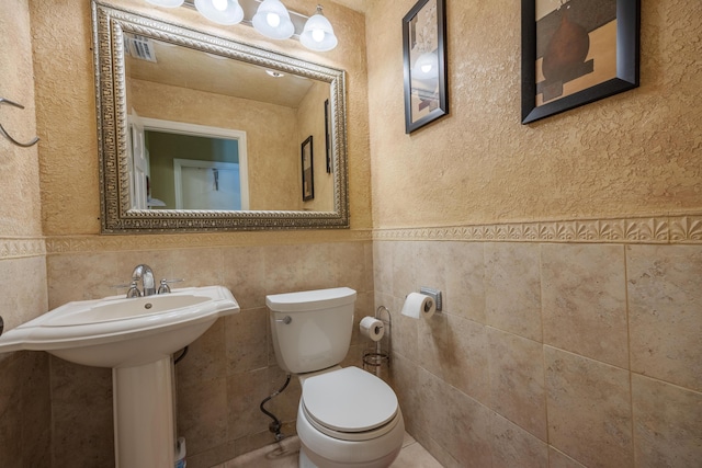 bathroom featuring toilet, sink, and tile walls