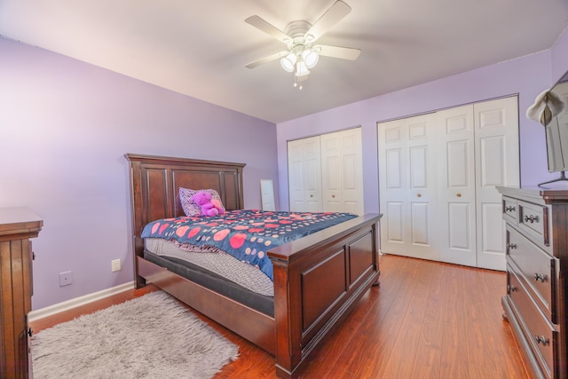 bedroom with two closets, hardwood / wood-style floors, and ceiling fan