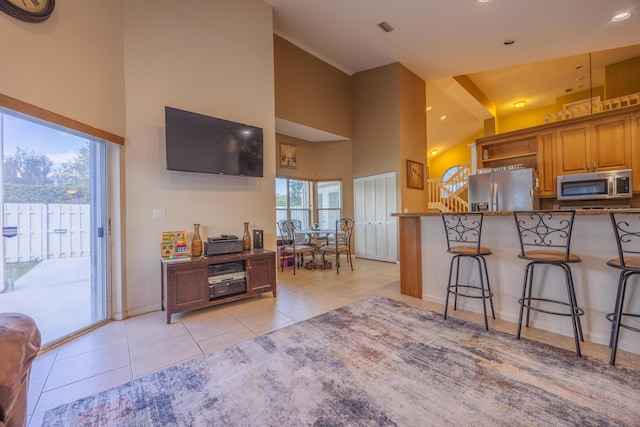 kitchen with appliances with stainless steel finishes, high vaulted ceiling, a kitchen breakfast bar, light tile patterned floors, and light stone countertops