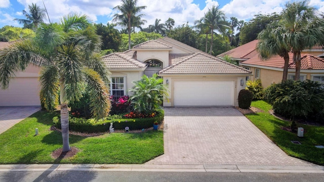 mediterranean / spanish-style house featuring a garage, a tiled roof, decorative driveway, stucco siding, and a front lawn