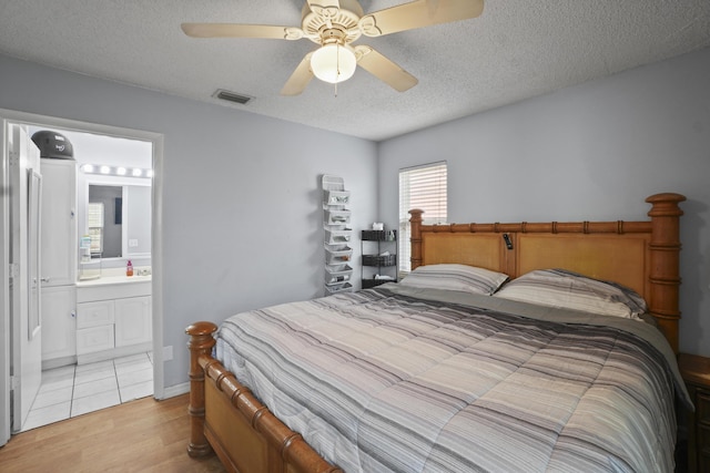 bedroom featuring a textured ceiling, connected bathroom, a ceiling fan, visible vents, and light wood-style floors