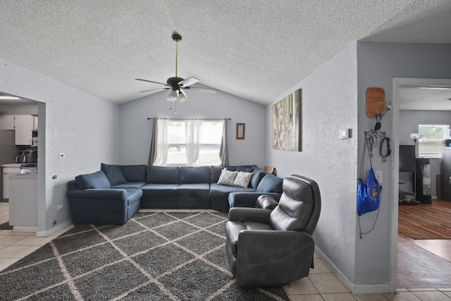 living area with light tile patterned floors, lofted ceiling, a textured wall, ceiling fan, and a textured ceiling