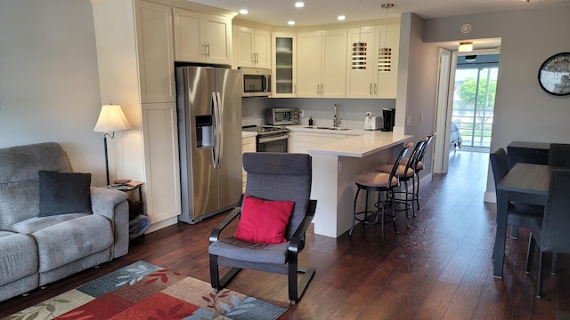 kitchen with dark hardwood / wood-style floors, a breakfast bar, sink, white cabinets, and stainless steel appliances