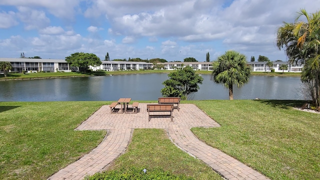 view of home's community with a water view, a lawn, and a patio area