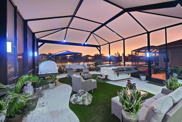 patio terrace at dusk with a lanai, outdoor lounge area, a yard, and a hot tub