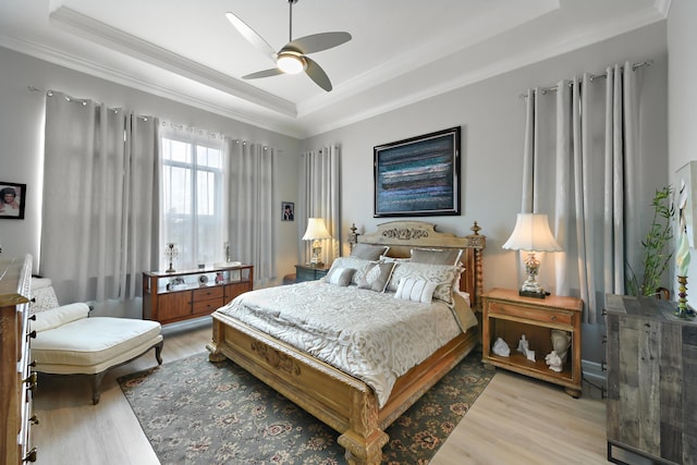 bedroom featuring a tray ceiling, ornamental molding, light wood finished floors, and ceiling fan