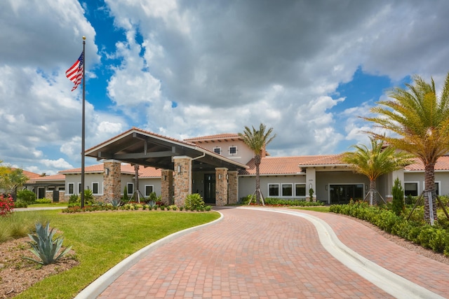 view of front facade featuring a tiled roof, stucco siding, a front lawn, and stone siding