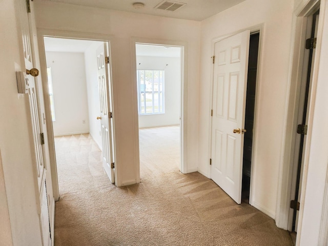 hall featuring light carpet, visible vents, and baseboards