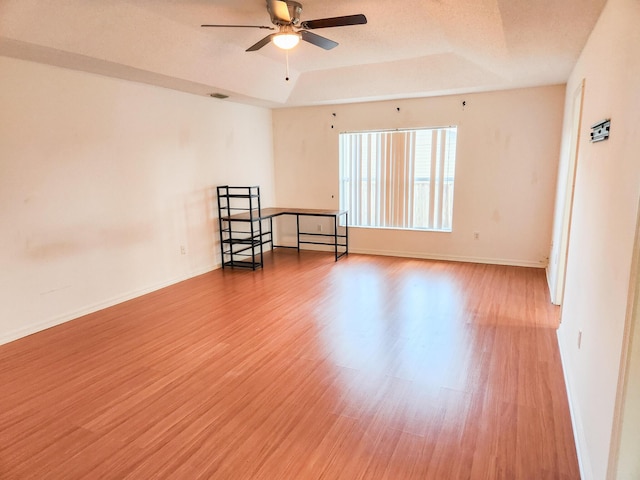 spare room with a tray ceiling, wood finished floors, baseboards, and ceiling fan