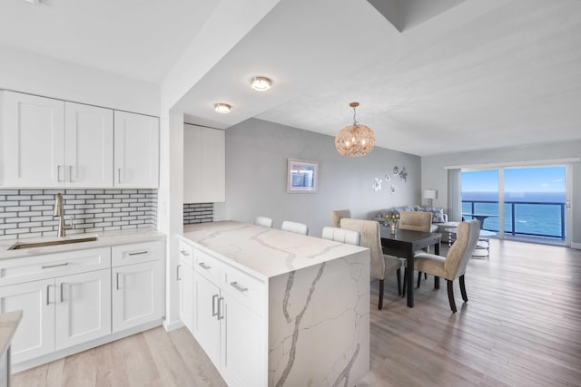 kitchen with a water view, kitchen peninsula, sink, and white cabinets