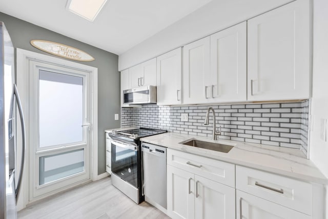 kitchen with white cabinetry, sink, light stone countertops, and appliances with stainless steel finishes