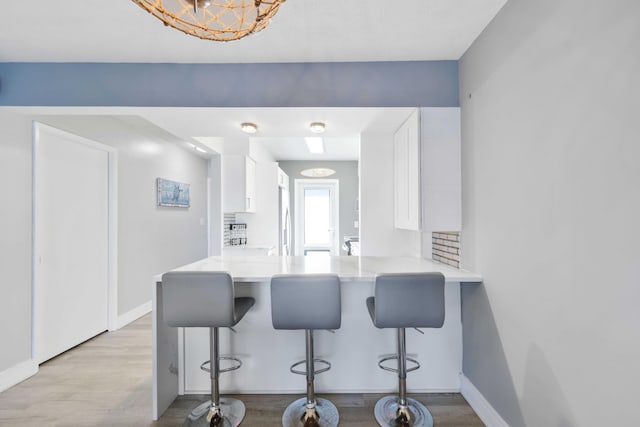 kitchen with a kitchen bar, kitchen peninsula, light wood-type flooring, and white cabinets