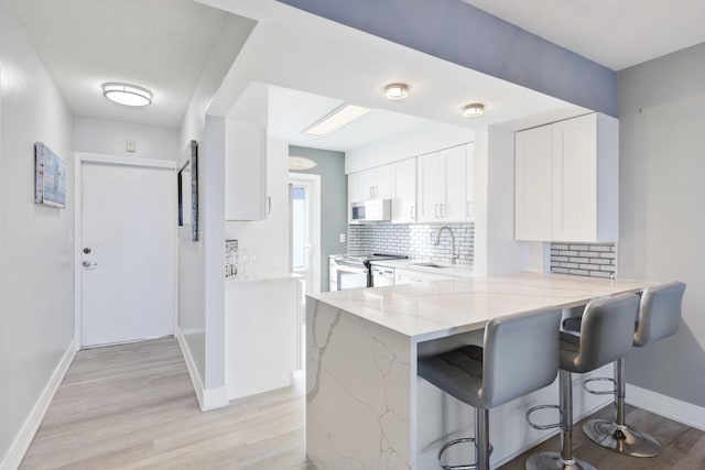 kitchen featuring stainless steel stove, light stone counters, white cabinets, a kitchen bar, and kitchen peninsula