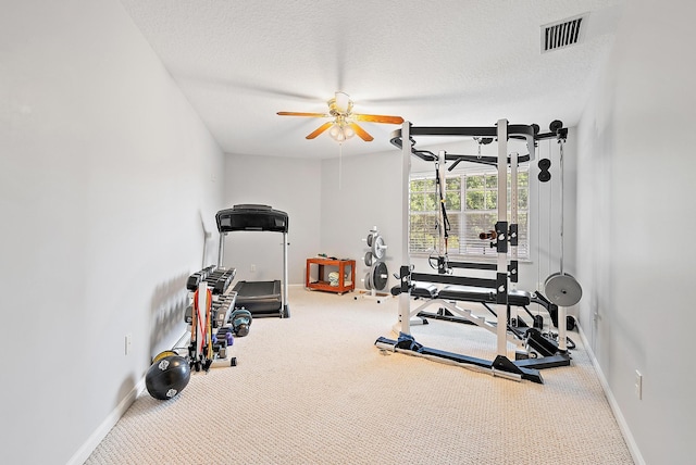 exercise area featuring ceiling fan, carpet flooring, and a textured ceiling