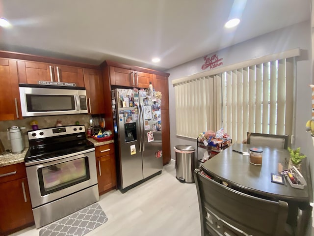 kitchen featuring appliances with stainless steel finishes, light wood-type flooring, and light stone countertops