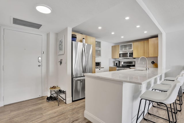 kitchen featuring appliances with stainless steel finishes, a breakfast bar, light brown cabinetry, sink, and kitchen peninsula