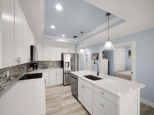 kitchen featuring sink, stainless steel appliances, a raised ceiling, and a center island with sink