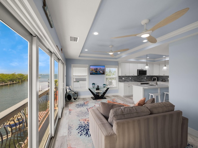 living room featuring a water view, sink, ceiling fan, and a tray ceiling