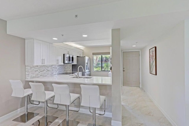 kitchen featuring appliances with stainless steel finishes, backsplash, white cabinets, a kitchen breakfast bar, and kitchen peninsula