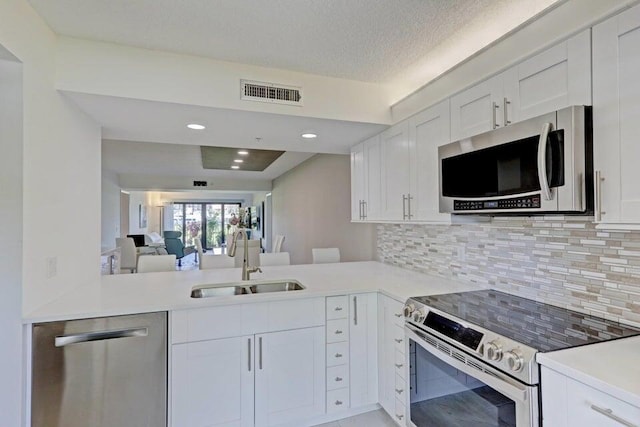 kitchen featuring sink, appliances with stainless steel finishes, white cabinetry, backsplash, and kitchen peninsula