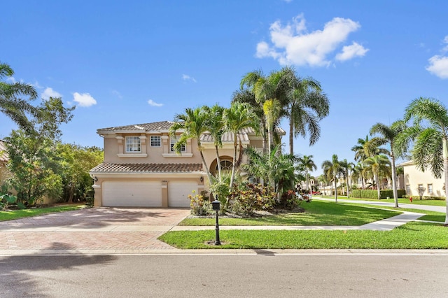 view of front of property with a tiled roof, an attached garage, decorative driveway, a front lawn, and stucco siding