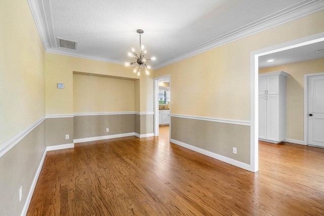 unfurnished room with crown molding, wood finished floors, visible vents, and a chandelier