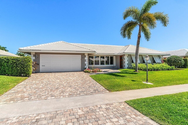 single story home featuring a tiled roof, a front yard, stucco siding, decorative driveway, and an attached garage