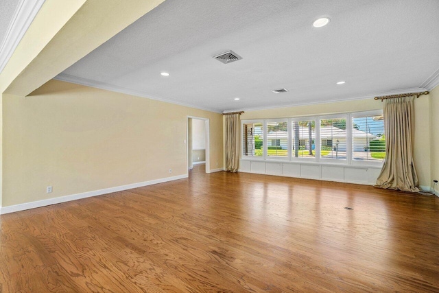 unfurnished living room with baseboards, wood finished floors, visible vents, and ornamental molding