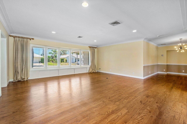 empty room with a chandelier, visible vents, crown molding, and wood finished floors