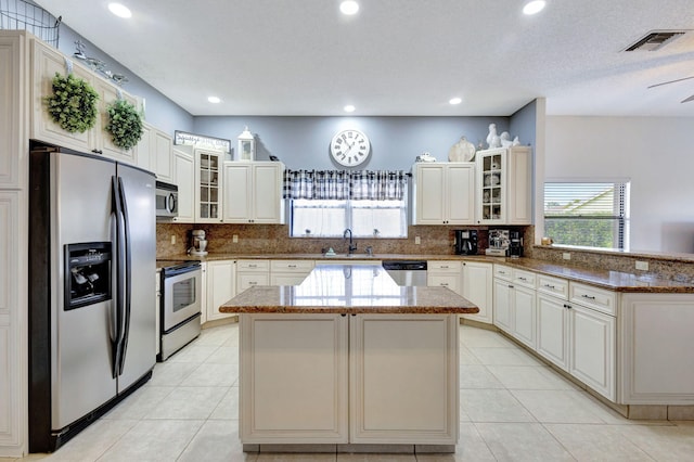 kitchen with light tile patterned floors, appliances with stainless steel finishes, dark stone countertops, a center island, and decorative backsplash