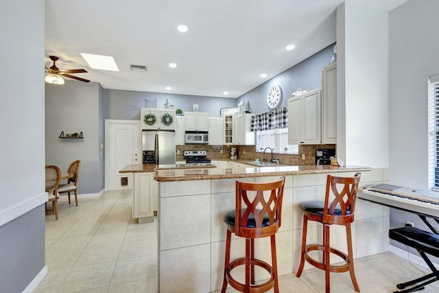 kitchen with a breakfast bar, light tile patterned floors, light stone counters, kitchen peninsula, and stainless steel appliances