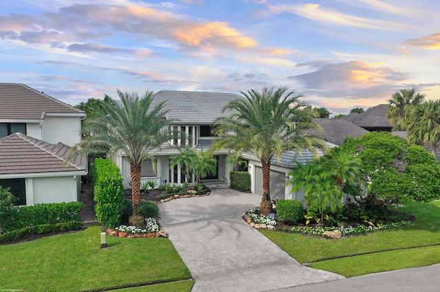 view of front of home with a garage, driveway, a tiled roof, stucco siding, and a front lawn