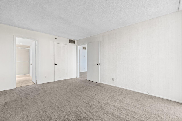 unfurnished bedroom featuring ensuite bath, carpet flooring, a closet, and a textured ceiling