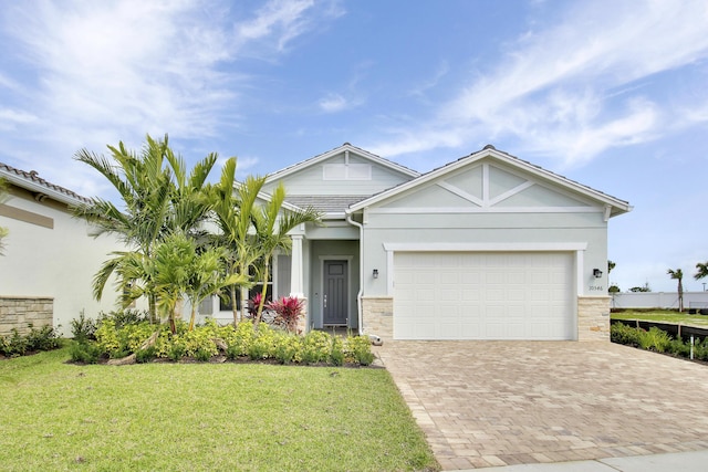 craftsman-style house featuring an attached garage, stucco siding, decorative driveway, and a front yard