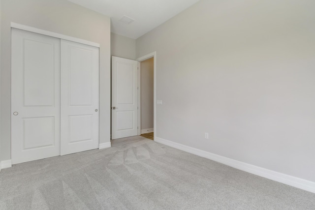 unfurnished bedroom with a closet, light colored carpet, and baseboards