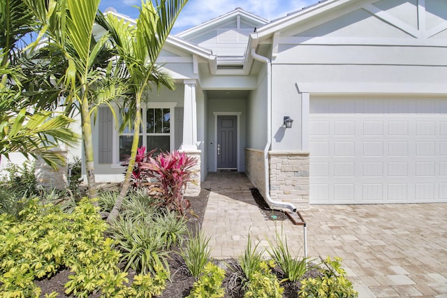 entrance to property with a garage, stone siding, and stucco siding