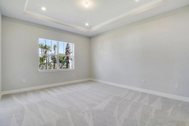 empty room with ornamental molding, a raised ceiling, light carpet, and baseboards