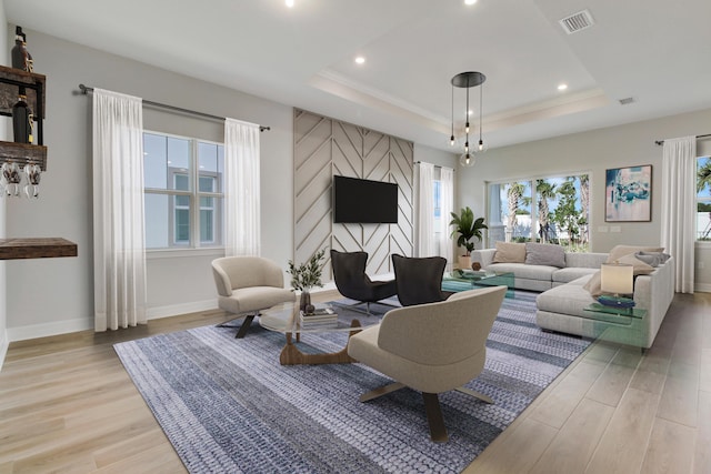 living area featuring light wood-type flooring, baseboards, visible vents, and a raised ceiling